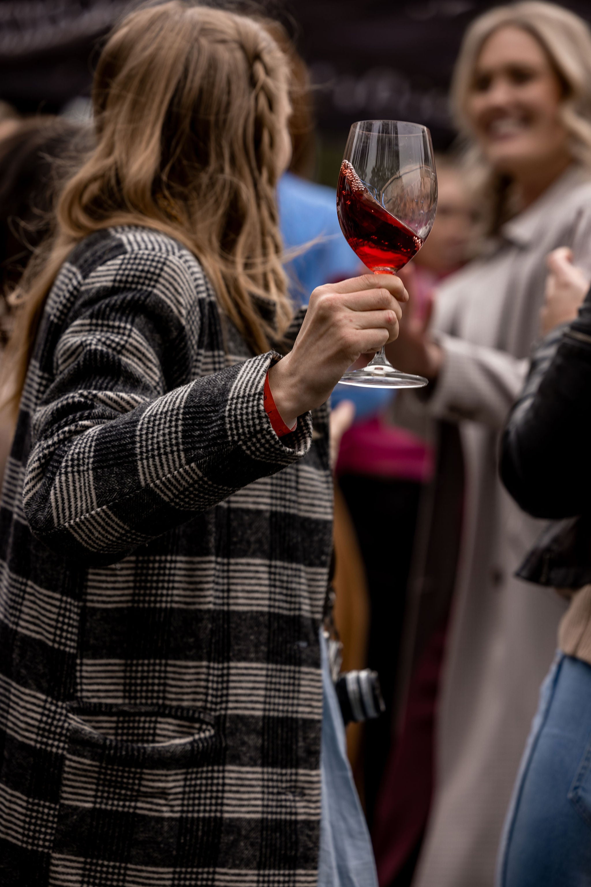 Person holding a glass of red wine with blurred people in the background